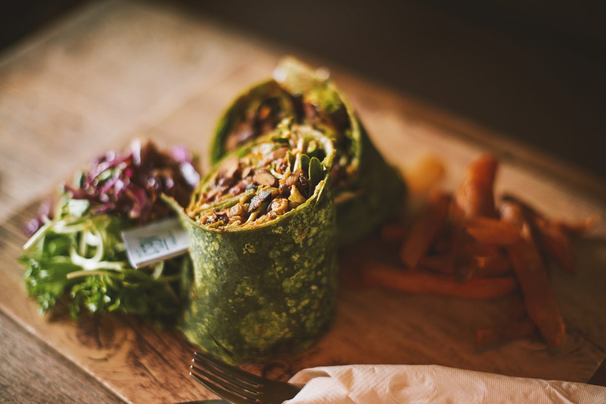 A green-tortilla wrap cut open, served on a wooden board.