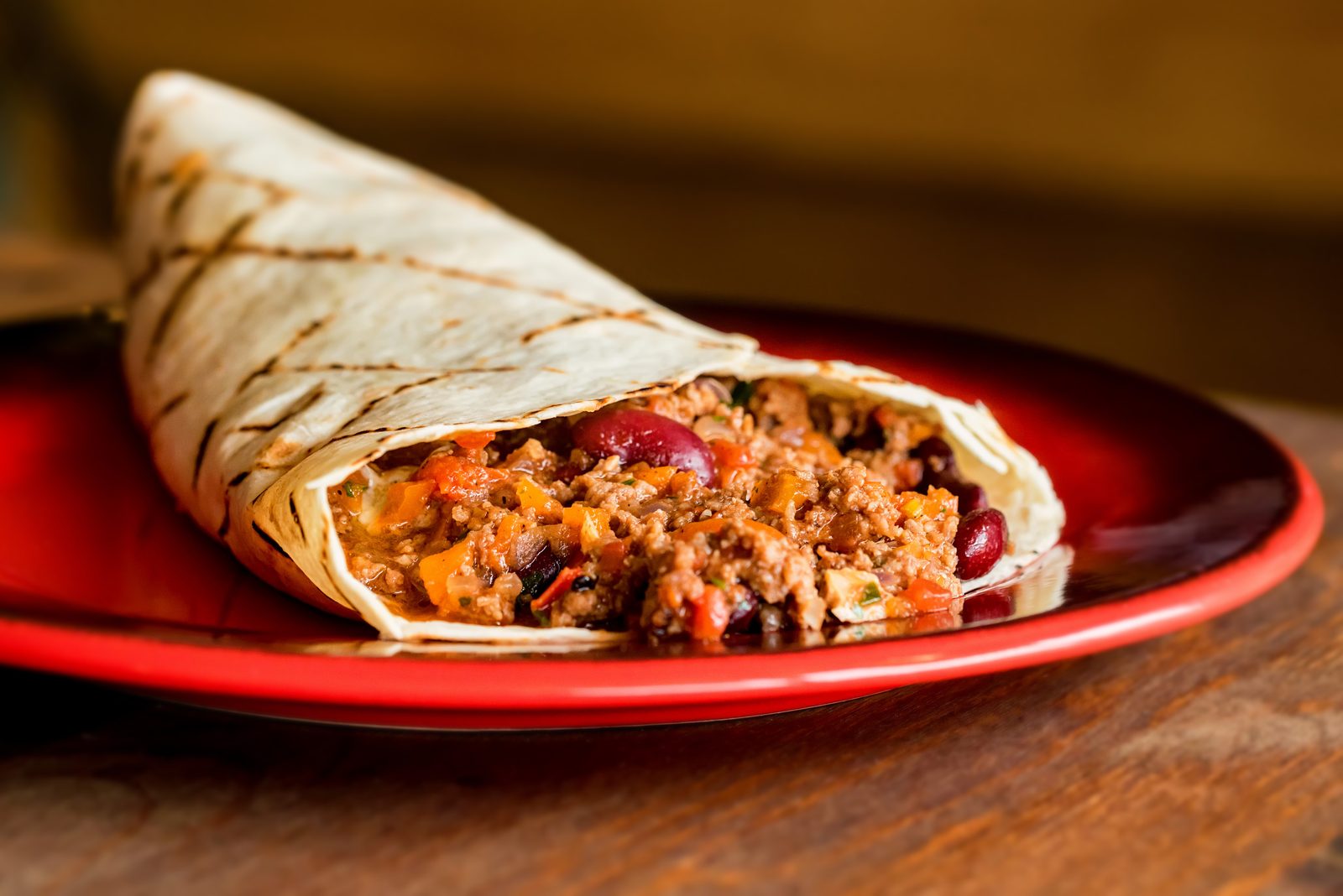 A burrito with minced meat and beans on a red plate.