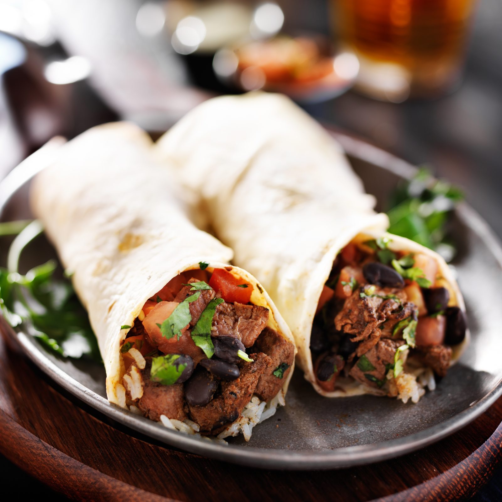 Two burritos with steak and black beans on a rustic plate.